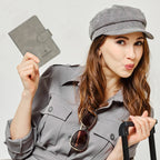 Grey passport wallet with fold-over strap, held up near travel outfit; gift? no