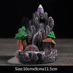 Resin landscape waterfall incense burner with green trees, orange-roof houses, and purple incense cone