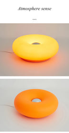 Two views of glowing donut table lamp: yellow top and orange side lighting