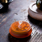 Amber glass incense vessel with orange patterned lid and smoke plume