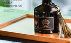 Dark glass reed diffuser bottle with label and gold tassel on wooden surface