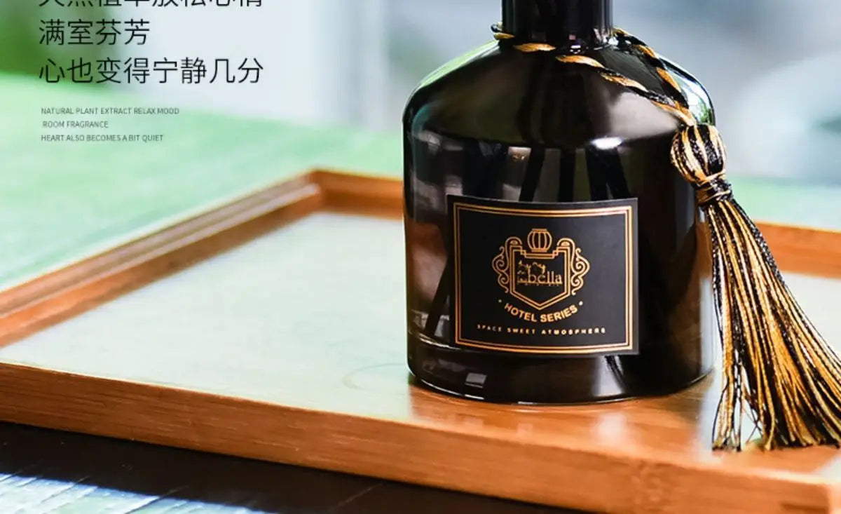 Dark glass reed diffuser bottle with label and gold tassel on wooden surface