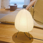 White paper lantern bedside lamp with black tripod legs and arched handle; unlit