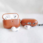 Orange and dark orange leather AirPods cases plus white earbuds, each with keychain ring