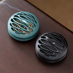 Blue-green and black incense burners side by side, round with oval cutout pattern