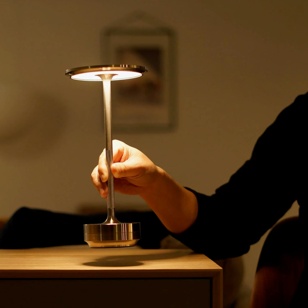 Hand touching a cordless touch table lamp with golden stem and round base