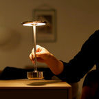 Hand touching a cordless touch table lamp with golden stem and round base