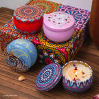 4 scented candle tins with colorful Arabian-style mandala lids and one lit flame