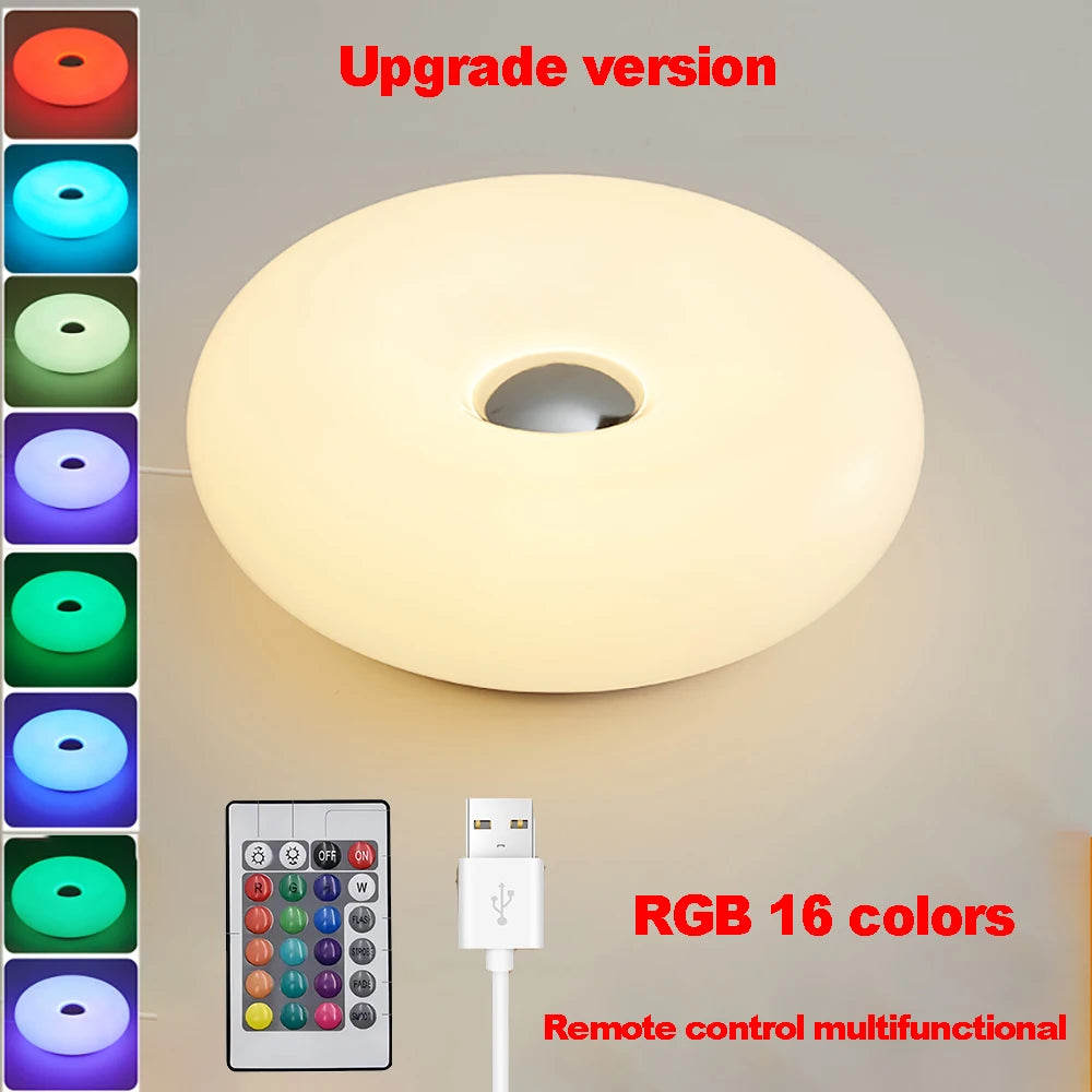 White donut table lamp glowing, with remote control and charging cable.