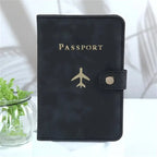 Passport cover in dark vegan leather with “PASSPORT” and airplane emblem, snap closure