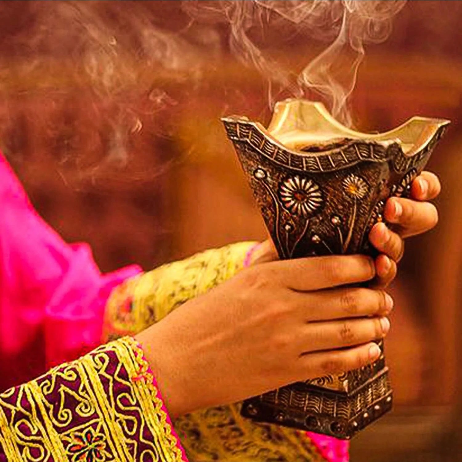 Burning bakhoor incense cone in ornate patterned holder held in hand