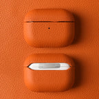 Orange leather AirPods case with textured finish, open lid, and small dot detail