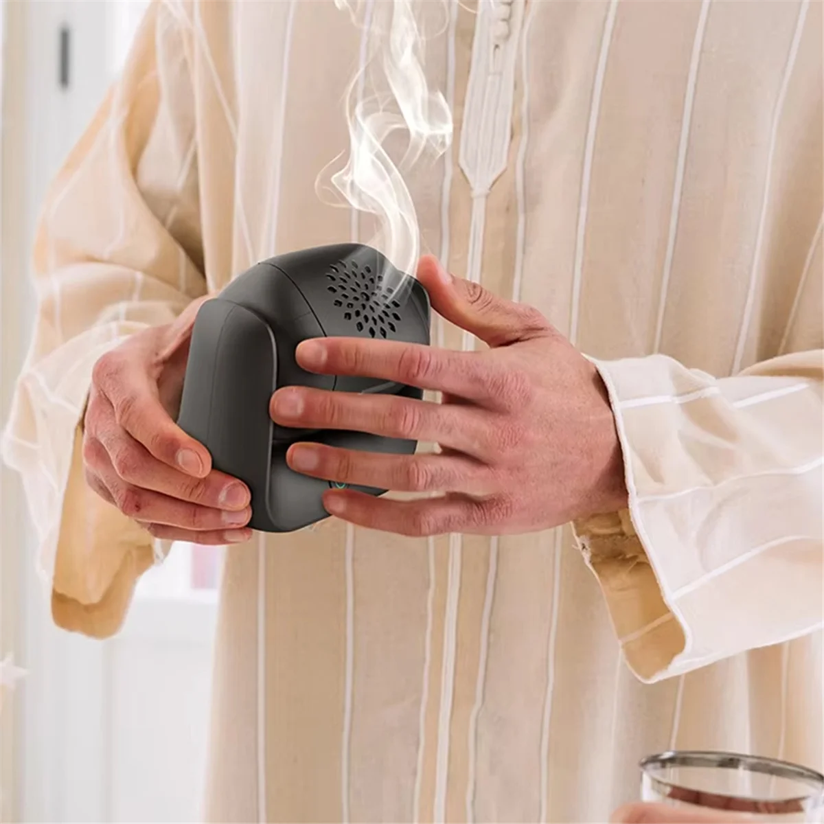 Rotatable electric bakhoor burner in hands, black device with vent holes and side grip