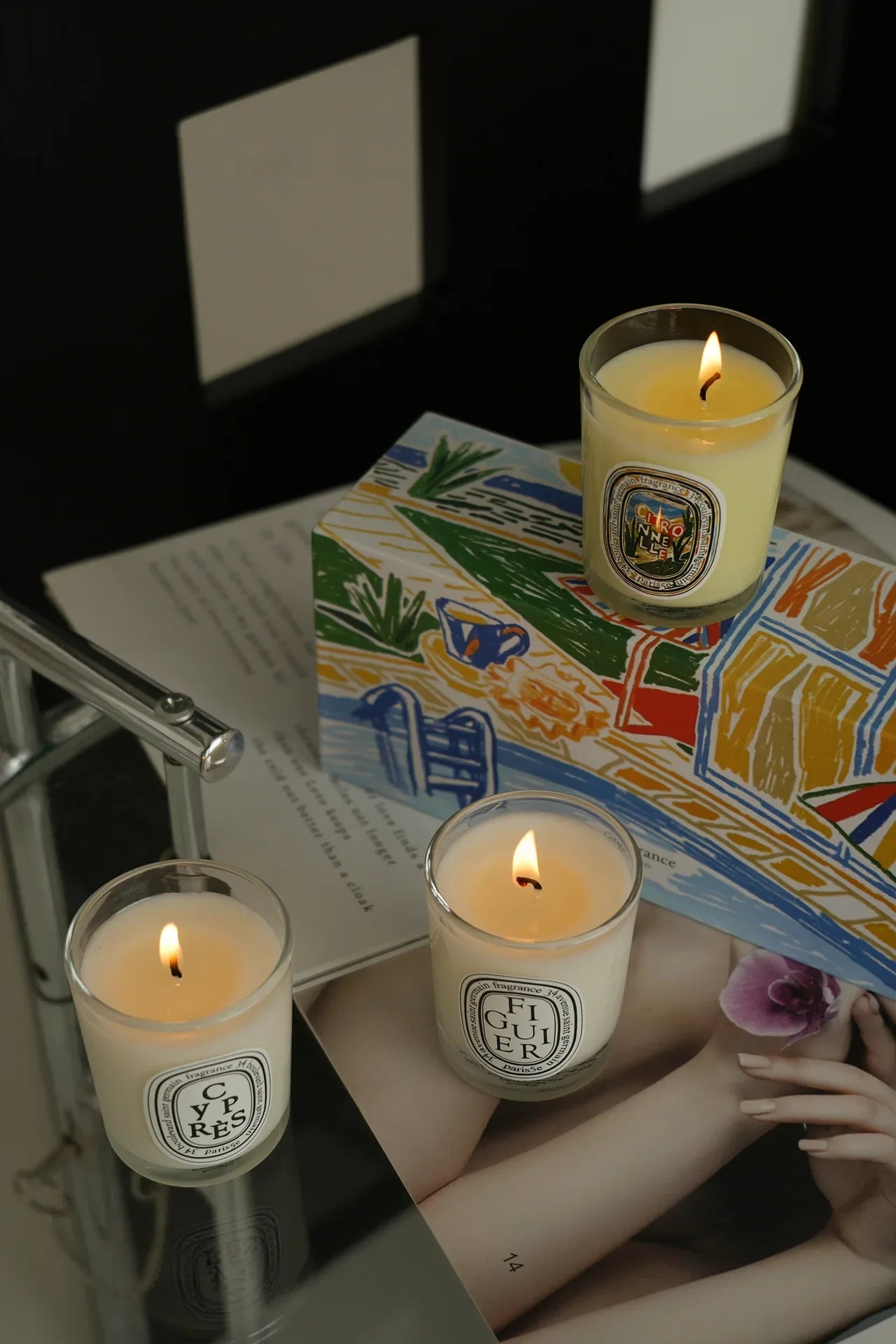 French Botanical lit candle jars on a patterned gift box, flames visible