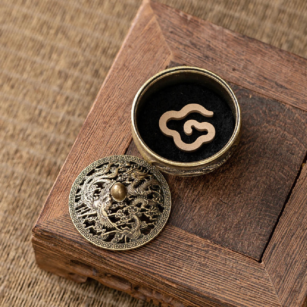Brass pocket incense burner with dragon-engraved lid and black insert with swirl symbol