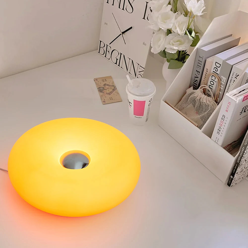 Warm yellow donut table lamp with center cutout, glowing on a desk