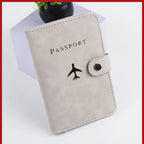 Light gray passport folio with airplane logo and side snap button closure, stitched trim