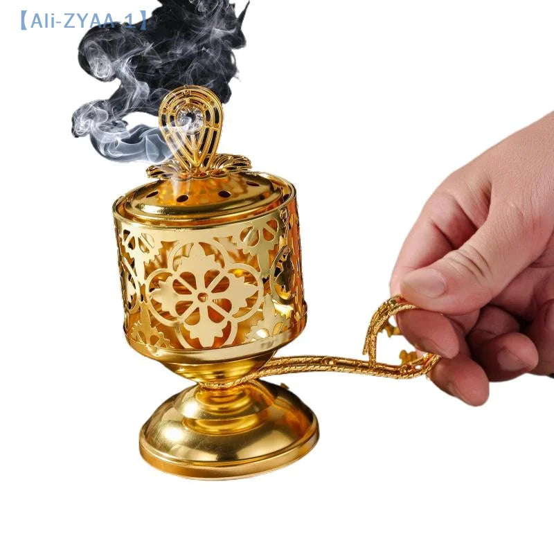 Arabesque incense burner in gold, pierced cylinder with ornate lid; hand holds the handle