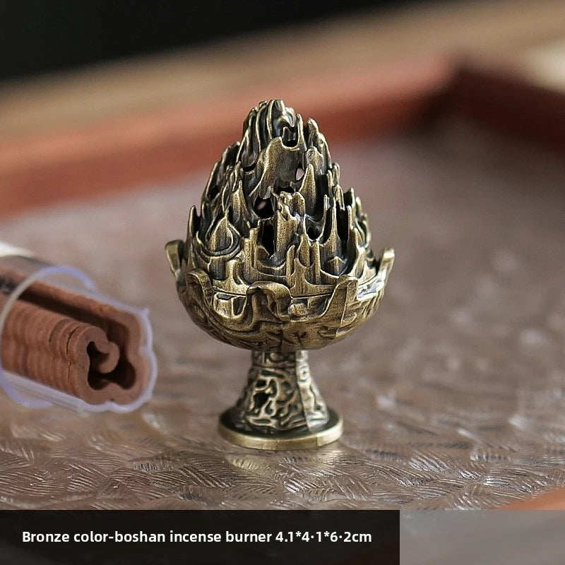 Bronze-and-gold boshan incense burner standing on a textured surface with smoke.