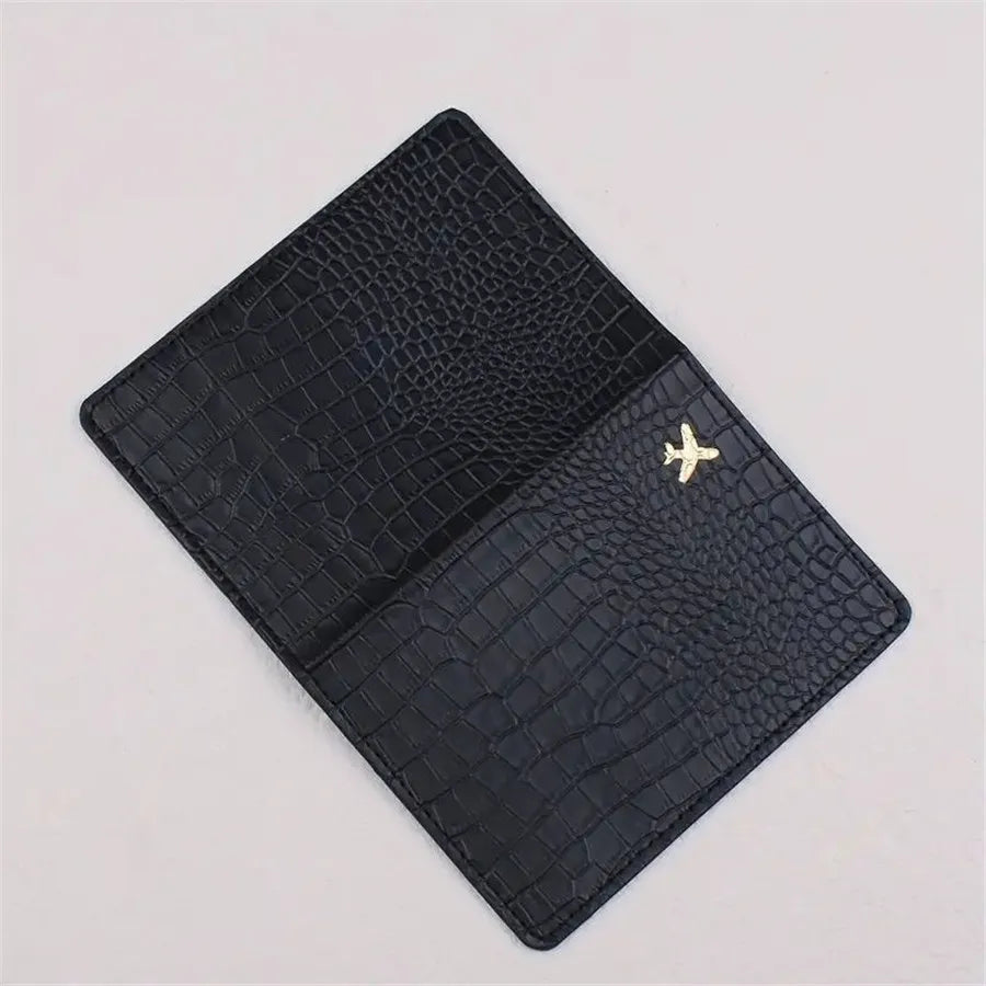 Black croc-embossed passport holder with gold airplane emblem on front