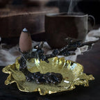 Gold-toned leaf incense bowl with dark plum-branch stand and burning cone holder