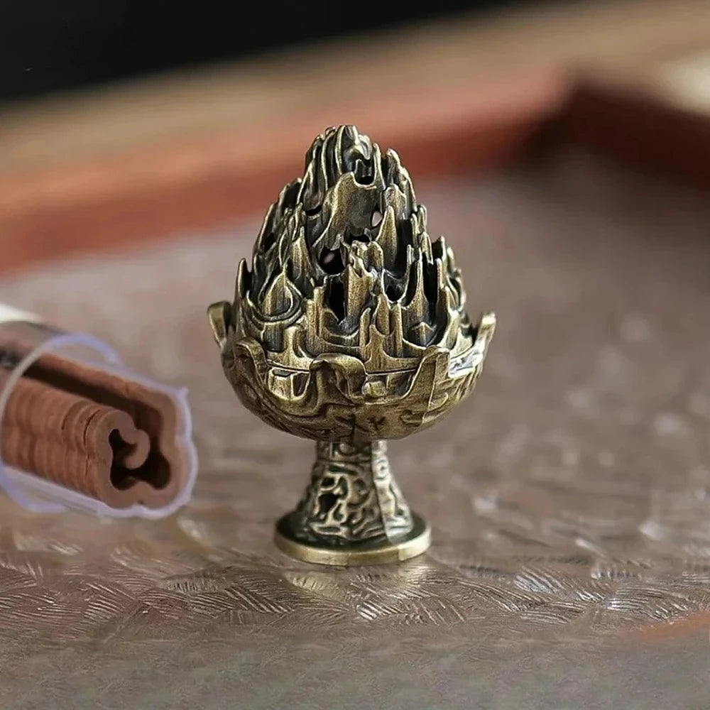Copper-toned incense burner cup with flame-lotus lid detail and pedestal base; smoke nearby.