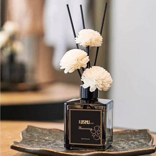 Mini reed diffuser bottle with black reeds and three white flower heads on tray