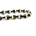 Close-up of black prayer beads with gold and white striped pattern, textured dots