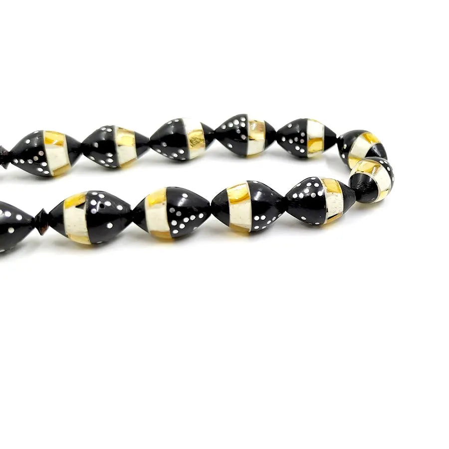 Close-up of black prayer beads with gold and white striped pattern, textured dots