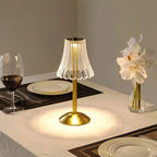 Cordless table lamp with pleated glass shade and gold base on bedside tabletop