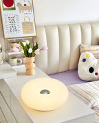 Soft white donut table lamp glowing, round body with center circular opening