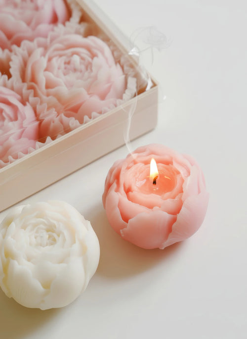 Rose-shaped soy wax candle with lit wick beside a pale rose candle in a box