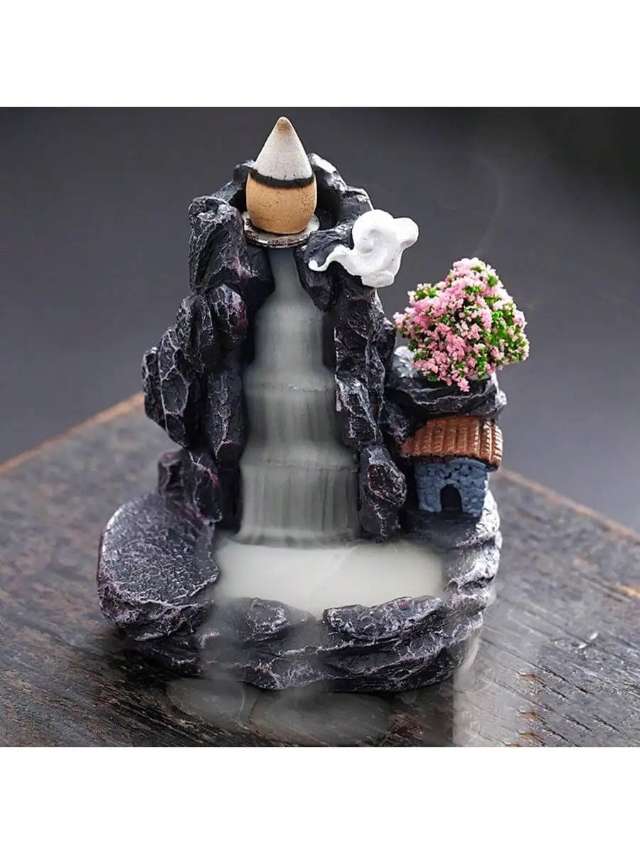 Backflow waterfall incense holder with white smoke and pink flowers beside stone arch