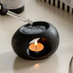 Black ceramic aroma oil burner with top oil reservoir and lit tea candle