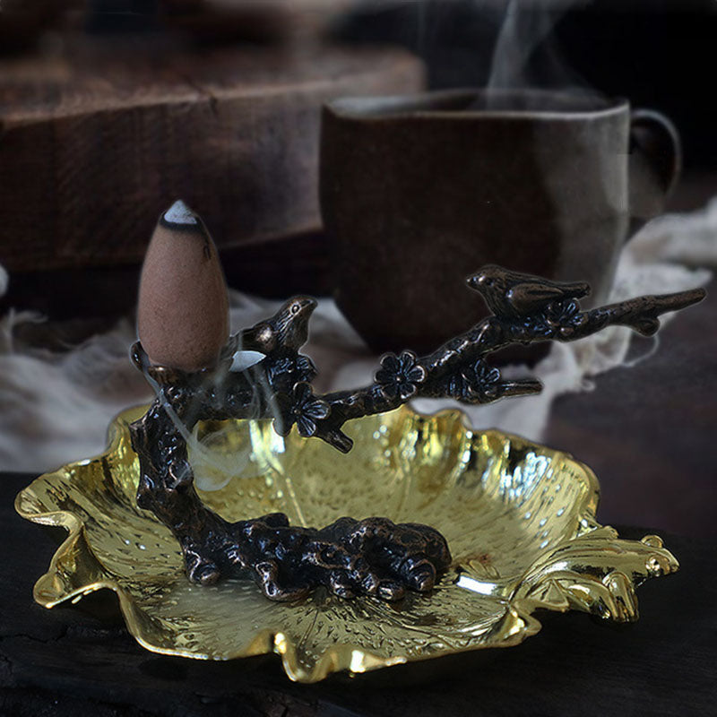Gold-toned leaf incense bowl with dark branch stand and burning cone incense