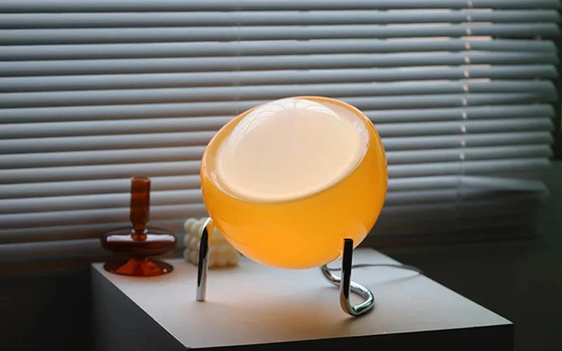 Amber glass globe lamp with warm internal light and chrome curved supports