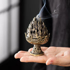 Copper-toned incense burner with flame-lotus top, held above an open hand; incense smoke.