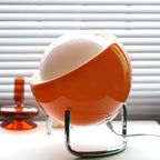 Orange glass globe table lamp with chrome stand and visible power cord near base