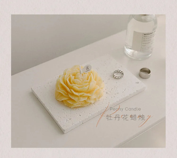 Yellow peony sculptural candle on a tray with ring and bottle nearby