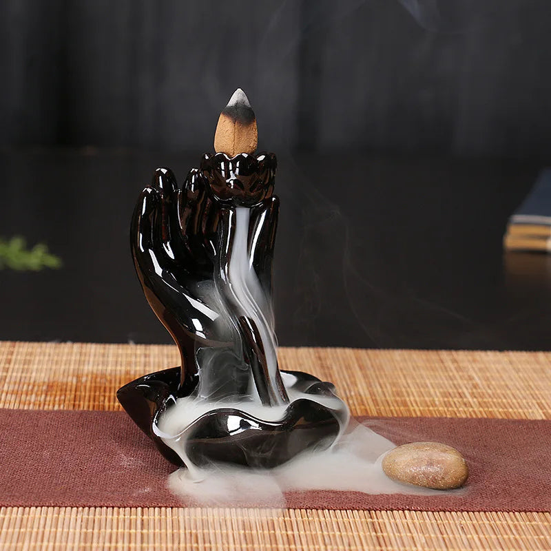 Black glossy backflow incense burner releasing smoke from a seated hand incense holder