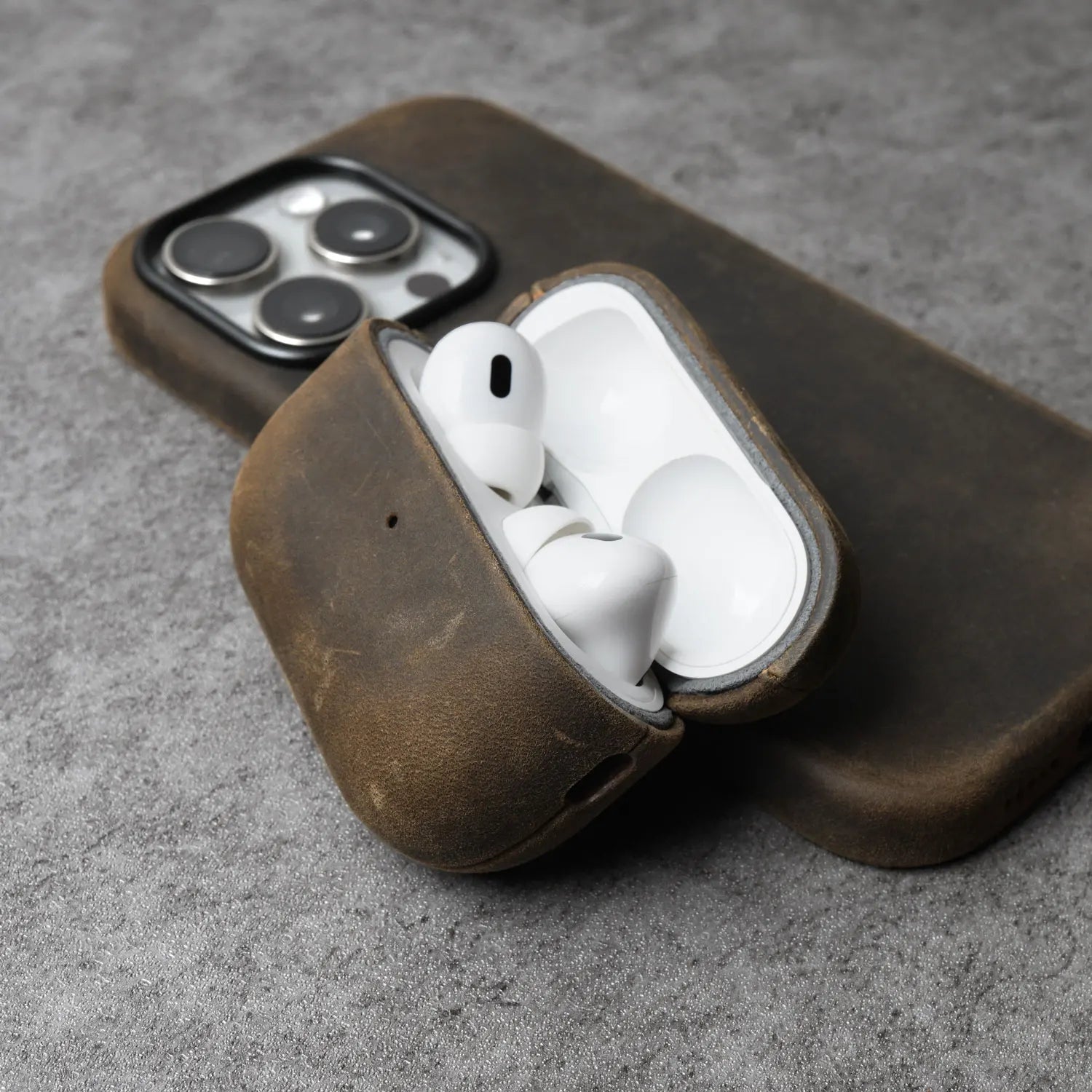 Brown leather AirPods case holding white earbuds, with lid opening and cutouts