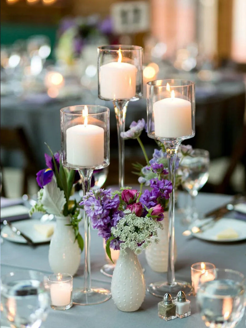 Trio of clear glass candle holders with lit candles in stemmed goblet cups