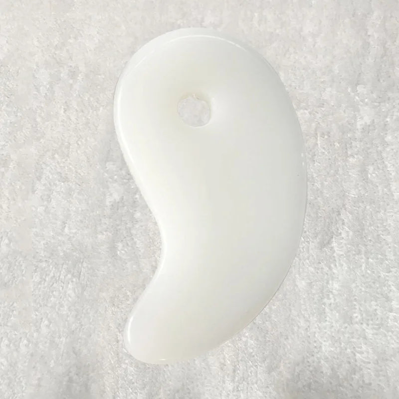 Ivory gua sha stone with glossy white, curved teardrop shape and small center hole.