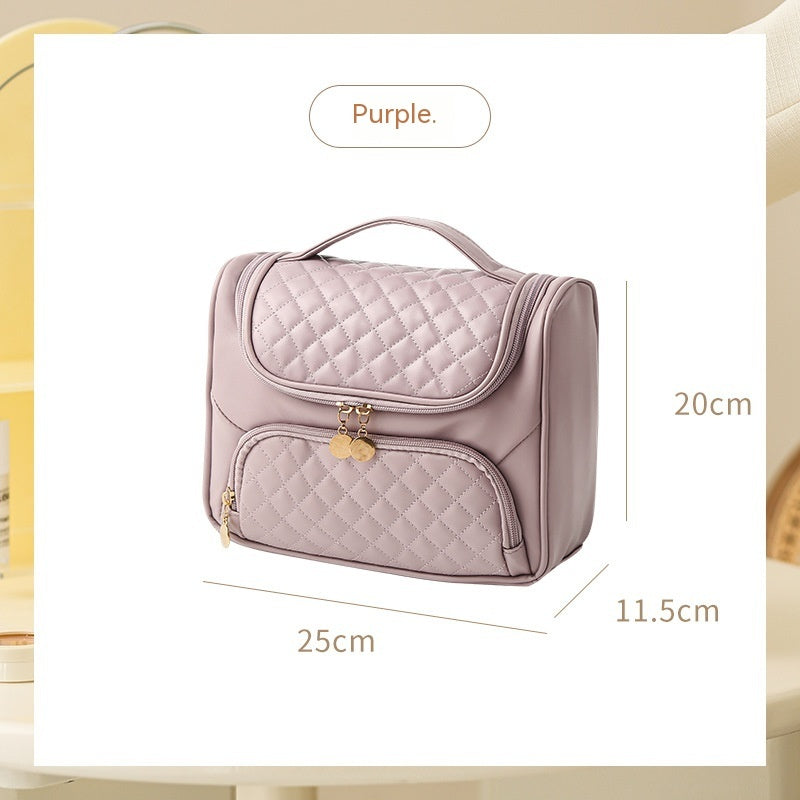 Purple quilted vanity bag with handle, front zip pocket, and coin charm zipper pulls.