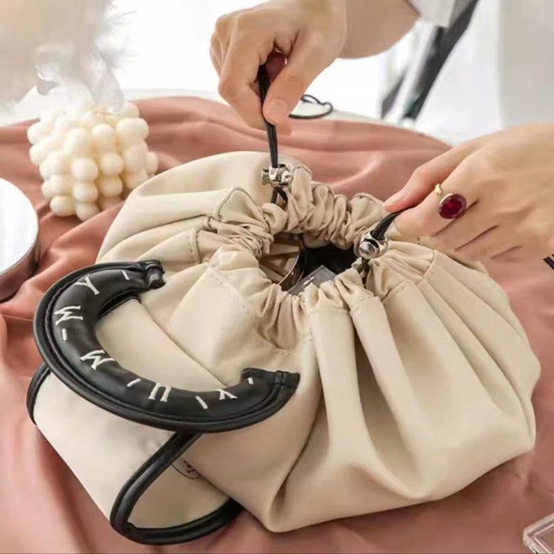 Cream drawstring wash bag with black oval loop handle and cinched open pouch
