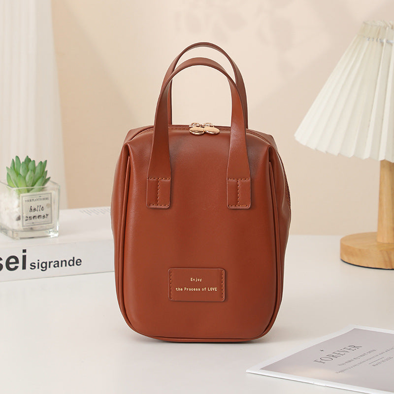 Brown travel vanity bag with top handles and front logo patch.