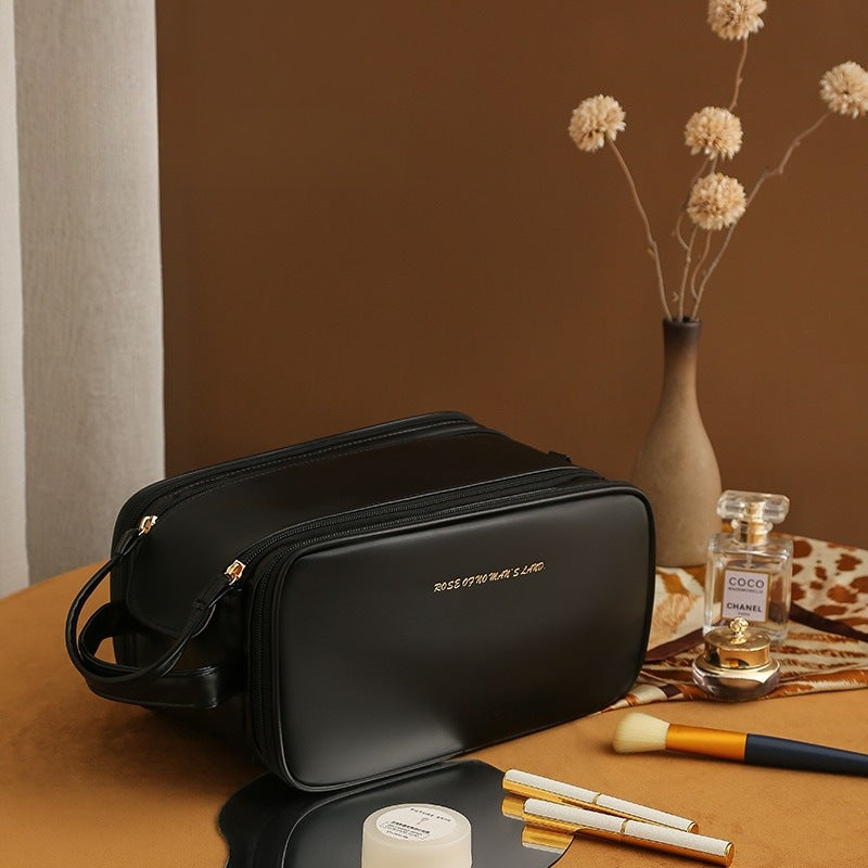 Black structured travel vanity case with zip closure and crossbody strap, front monogram