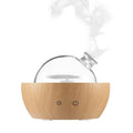 Nebula glass aroma diffuser releasing mist from clear glass globe on light wood grain base