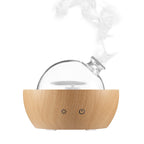 Nebula glass aroma diffuser releasing mist from clear glass globe on light wood grain base
