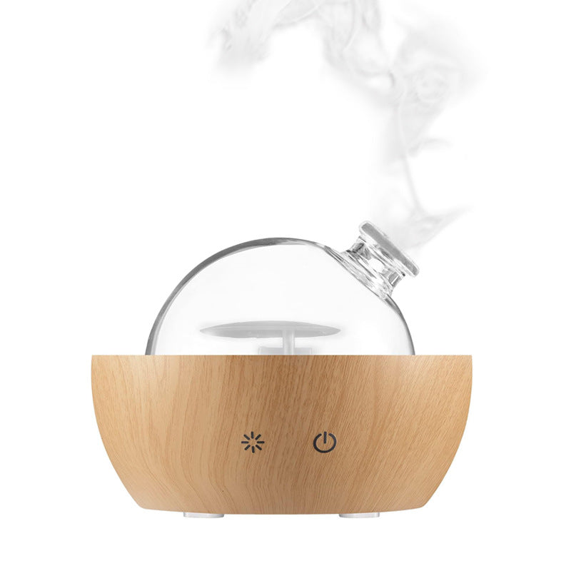 Nebula glass aroma diffuser releasing mist from clear glass globe on light wood grain base